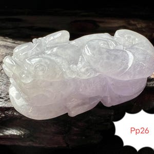 Könnte beinhalten: Eine durchscheinende, geschnitzte Jadefigur in Weiß- und Lavendeltönen. Die Skulptur zeigt eine Fabelwesen mit detaillierten Merkmalen. Die Basis der Figur ruht auf einer dunklen Oberfläche. Der Text "Pp26" befindet sich in einer weißen Blase.
