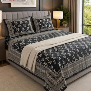 May include: A black bed sheet set featuring a cream-colored leaf pattern and a decorative border, including two matching pillowcases and a solid cream-colored throw blanket draped across the bed. The text "SKIN FRIENDLY COTTON" is visible.