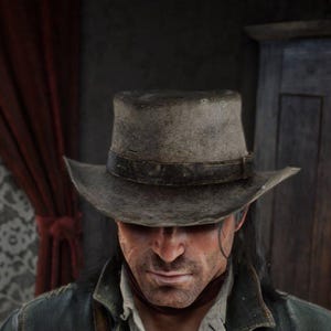 May include: A weathered gray cowboy hat with a dark leather band. The hat is worn and has a slightly curved brim. The person wearing the hat is looking down, with a serious expression.