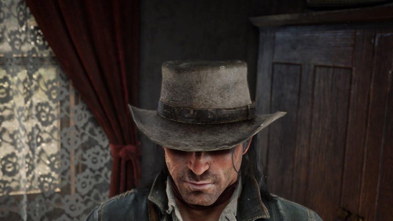 May include: A weathered gray cowboy hat with a dark leather band. The hat is worn and has a slightly curved brim. The person wearing the hat is looking down, with a serious expression.