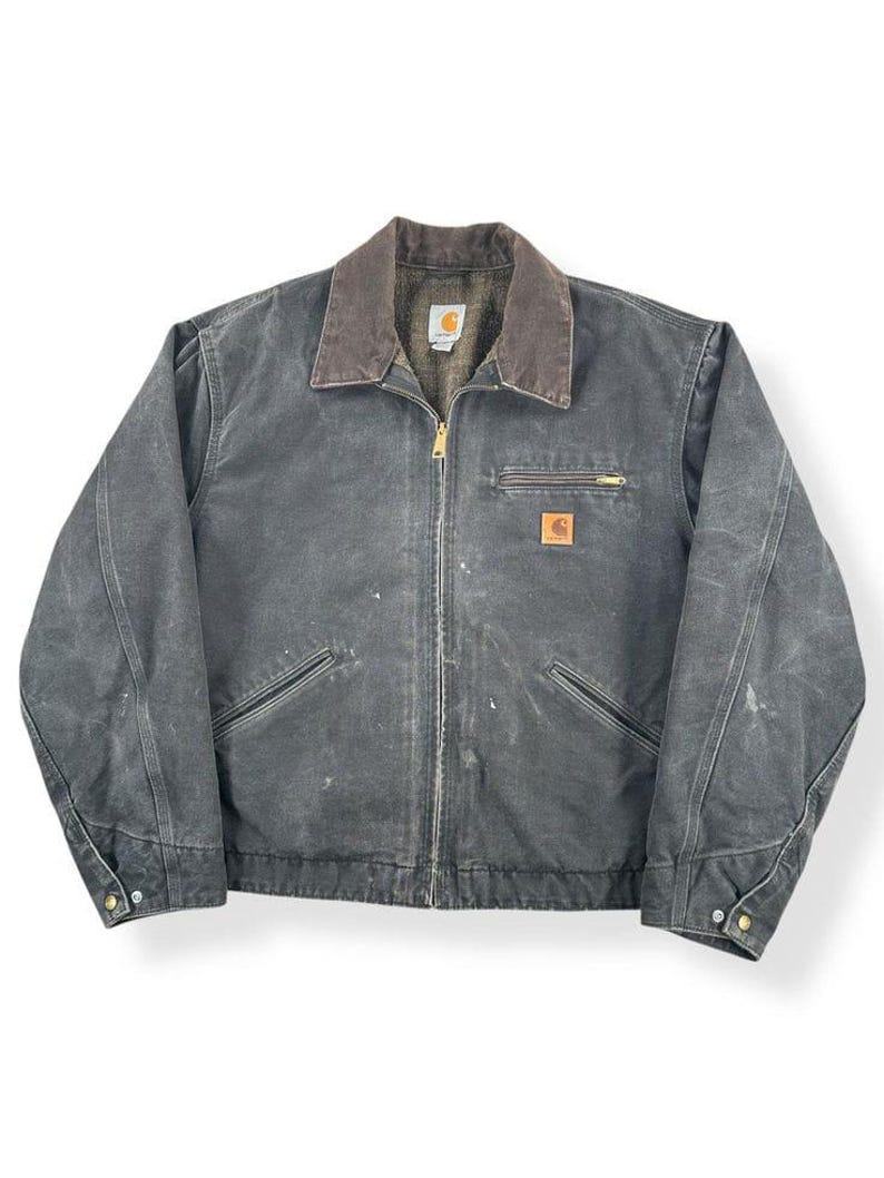 May include: A charcoal-colored work jacket with a brown corduroy collar. The jacket features a full zipper, multiple pockets, and a small logo patch. The jacket has a worn appearance, suggesting it is pre-owned.