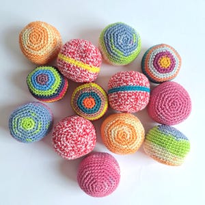 Puede incluir: Una colección de trece pequeñas bolas redondas de ganchillo en varios colores y patrones. Las esferas presentan texturas de hilo intrincadas con diseños que incluyen rosa sólido, naranja, rayas multicolores y patrones circulares concéntricos.