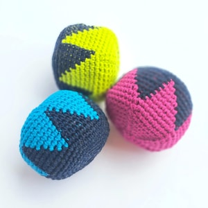 Peut inclure: Trois balles de jonglage crochetées et arrondies présentant un motif géométrique bicolore. Chaque balle associe un fil gris anthracite foncé à une couleur vive : une jaune néon, une bleu turquoise vif et une rose fuchsia.