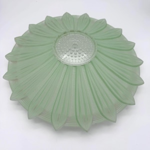 May include: A round, pale green glass ceiling light shade featuring a raised, petal-like floral design radiating from a central, clear, textured glass circle. The glass has a frosted finish with defined ridges along each petal shape.