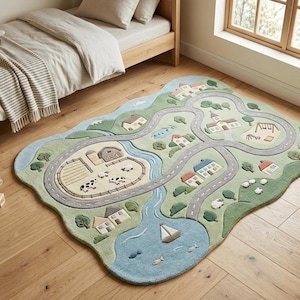 May include: A rectangular area rug with rounded edges featuring a colorful town and country scene. The design includes a winding gray road, a blue river with a sailboat, a farm with cows, houses, trees, and a playground, all in shades of green and blue.