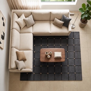 May include: An overhead shot of a contemporary living room featuring a cream-coloured sectional sofa and a dark grey rug with a grid design. A wooden coffee table holds decorative items. Neutral-toned cushions add colour. A potted plant is in the corner.