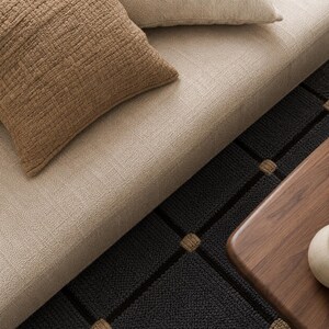 May include: An overhead view of a living room arrangement featuring a beige sofa with brown textured cushions. A black patterned rug and a wooden side table are also present, contributing to a comfortable interior.