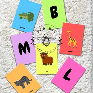 May include: Colorful flashcards with animal illustrations and corresponding letters. The cards feature an alligator, a giraffe, a jaguar, and a yak. The cards are arranged on a white, textured surface. The text "PRAIRIE TEMPLATES CO." is also visible.