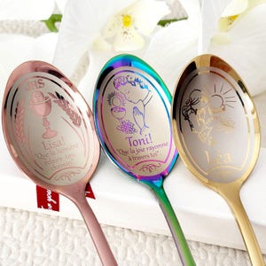 Könnte beinhalten: Drei dekorative Löffel mit eingravierten Designs. Einer ist roségoldfarben mit einem Kelch und Text, ein anderer ist irisierend mit einem betenden Kind, und der dritte ist goldfarben mit Sonne und Engel. Jeder Löffel hat einen Namen.