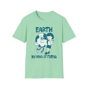 May include: A light green t-shirt with the words "EARTH" and "MY KIND OF FRIEND" in dark blue. The graphic shows a smiling Earth hugging a person. The t-shirt is made of a soft material.
