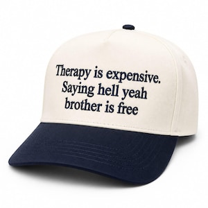Może przedstawiać: Czapka bejsbolowa z kremową koroną i granatowym daszkiem. Czapka ma haftowany granatowy napis: "Therapy is expensive. Saying hell yeah brother is free."