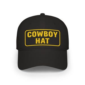 May include: Black baseball cap with a curved brim. The front of the cap features the words "COWBOY HAT" in yellow, inside a yellow rectangular border. The hat is a classic style, suitable for casual wear.