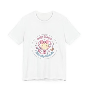 May include: White t-shirt with a circular design. The design features a smiling face, stethoscope, and the words "Soft Heart, Steady Hands." It includes a pink bow, hearts, and a bandage. The shirt is made of a soft material.