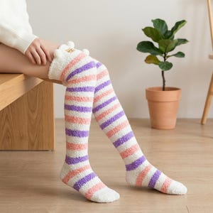 May include: Fluffy over-the-knee socks with pink, purple, and white stripes. The socks have a decorative trim at the top. The knee-high socks are made of a soft, fuzzy material. The socks are designed to be worn over the knee.