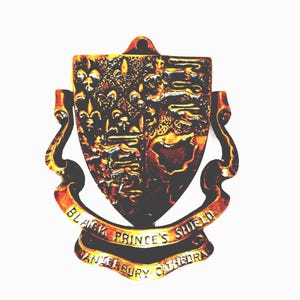 May include: A metallic door knocker shaped like a shield featuring the Black Prince's Shield design. The shield displays fleur-de-lis and lion motifs. A curved banner at the bottom reads "BLACK PRINCE'S SHIELD" and "CANTERBURY CATHEDRAL".
