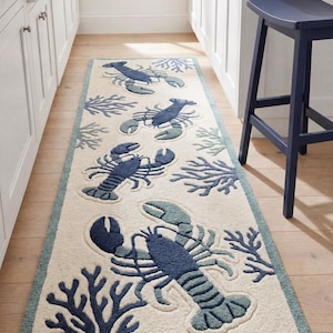 May include: A cream-coloured rectangular rug with a repeating pattern of navy and teal lobsters and coral. The rug has a teal border and is placed on a wooden floor.