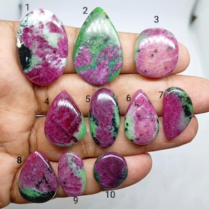 May include: Ten polished ruby zoisite gemstones in various shapes and sizes, labeled with numbers one through ten. Each stone features a unique combination of vibrant magenta, deep green, and black mineral inclusions with a smooth, glossy finish.