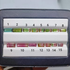 Puede incluir: Una colección de quince piedras preciosas rectangulares de corte baguette dispuestas en dos filas dentro de un estuche. Las piedras muestran un degradado de colores que incluye azul verdoso, verde lima, oliva, rosa y combinaciones bicolores.