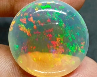 Könnte beinhalten: Ein runder, polierter Opal-Edelstein. Der Opal zeigt ein lebendiges Farbspiel mit grünen, roten, orangefarbenen und gelben Farbtönen. Der Edelstein ist vor einem dunklen Hintergrund platziert.