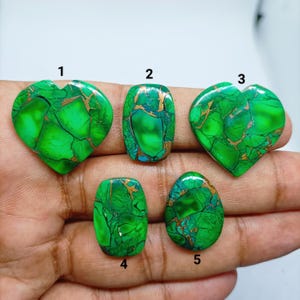 May include: Five polished green stones with copper-colored veining, labeled 1 through 5. Two stones are heart-shaped, two are rectangular with rounded corners, and one is teardrop-shaped. The stones display vibrant green hues and intricate patterns.