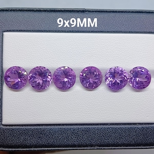 May include: Six round, faceted purple gemstones arranged in a horizontal row. Each stone measures 9x9mm as indicated by the text above. The gems are set against a white textured background within a dark blue case, displaying a vibrant violet hue.