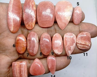 以下が含まれることがあります： 楕円形、長方形、涙型、不規則な形など、さまざまな形とサイズの14個の研磨されたロードクロサイトのカボションのコレクション。各石は、滑らかな仕上げで、独特のピンクと白の縞模様を示しています。