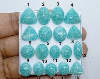 May include: A collection of eighteen polished, light teal amazonite gemstones arranged in a white display tray. The stones feature various shapes including ovals, triangles, and a marquise cut, each marked with a corresponding black number.