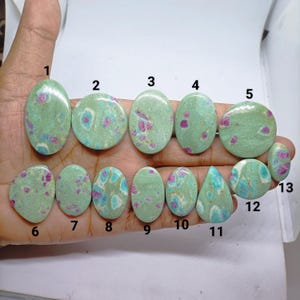 Peut inclure: Treize pierres précieuses cabochons polies disposées sur deux rangées, présentant une base vert clair avec des inclusions rose vif et bleu. Chaque pierre est numérotée de 1 à 13, avec des formes ovales, rondes et en goutte d'eau lisses.
