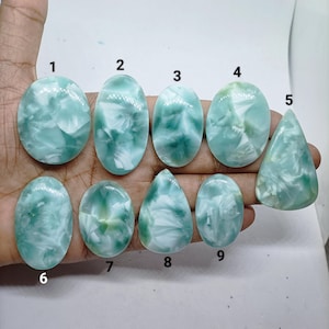 Può includere: Una collezione di nove cabochon levigati e lisci, di forma ovale e a goccia, caratterizzati da un motivo marmorizzato nei toni dell'azzurro, del verde acqua e del bianco. Ogni pietra è numerata da uno a nove, con distinte sfumature.