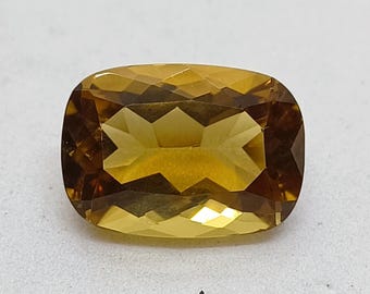 Op de afbeelding: Een edelsteen in kussenslijpvorm met een levendige goudgele tint en een gefacetteerd oppervlak. De steen vertoont een heldere, transparante kwaliteit met geometrische lichtreflecties over de gepolijste bovenkant en een rechthoekige vorm.