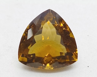 May include: A faceted, trillion-cut gemstone with a deep golden-yellow and amber hue. The stone features a triangular shape with sharp, pointed corners and a complex arrangement of internal geometric facets that reflect light across its surface.