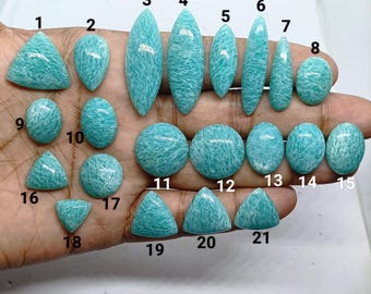 May include: A collection of twenty-one polished, light teal amazonite gemstones in various shapes including triangles, ovals, circles, and marquise cuts. Each stone is numbered from 1 to 21, displaying a unique, mottled white and teal pattern.
