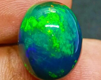 Könnte beinhalten: Ein polierter, ovaler schwarzer Opal-Edelstein. Der Opal zeigt ein lebendiges Farbspiel mit Grüntönen, Blau und einem Hauch von Gelb. Der Edelstein ist vor einem neutralen Hintergrund platziert, der seine natürliche Schönheit und einzigartigen Farbvariationen hervorhebt.