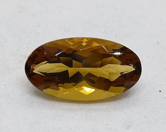 May include: An oval-cut gemstone with a vibrant golden-yellow and deep amber hue. The stone features a faceted surface that creates intricate geometric light reflections across its transparent body, showcasing a clear and polished appearance.