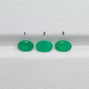 Pode incluir: Três pedras preciosas de cor verde vibrante com formato oval dispostas em uma linha horizontal. Cada pedra é marcada com um número preto acima, especificamente 1, 2 e 3, indicando peças individuais para seleção ou identificação.