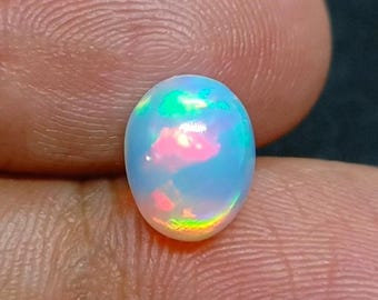 Könnte beinhalten: Ein ovaler Opal-Cabochon-Edelstein mit einer durchscheinenden weißen Basis und lebhaften, irisierenden Farbabstufungen in leuchtendem Pink, Neongrün und Elektroblau, präsentiert in einer glatten, polierten Oberfläche.