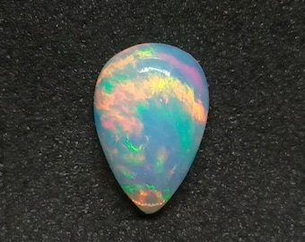May include: A teardrop-shaped opal gemstone exhibiting a kaleidoscope of colours. The stone features blues, greens, oranges, and pinks, set against a milky white background. The gemstone is presented on a dark, textured surface.