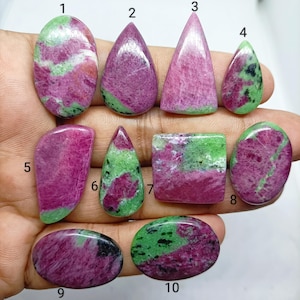 May include: Ten polished ruby zoisite cabochons in various shapes including oval, teardrop, triangular, and rectangular forms. Each stone displays a mottled pattern of vibrant magenta-pink ruby and deep green zoisite, labeled with numbers 1 through 10.