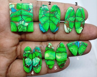 Op de afbeelding: Assortiment van gepolijste edelsteen cabochons in verschillende vormen. De stenen hebben een levendige groene kleur met blauwe en gouden accenten. De cabochons worden gepresenteerd op een neutrale achtergrond, die hun unieke patronen en texturen benadrukt.