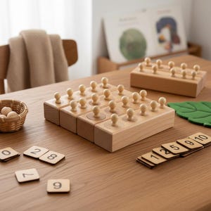 Puede incluir: Juego de juguetes educativos de madera con un tablero de clavijas, clavijas de madera, fichas de números y una pequeña cesta de bolas de madera. El juego está dispuesto sobre una mesa de madera de color marrón claro. También hay una pieza de fieltro verde en forma de hoja.