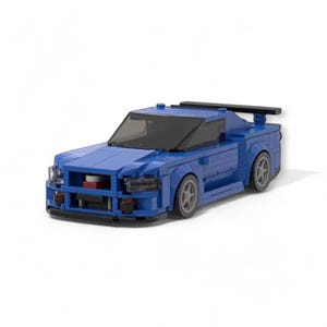 May include: A blue toy car constructed from interlocking blocks. The model features a spoiler, tinted windows, and grey wheels. The front of the car has red and black detailing. The car is set against a white backdrop.