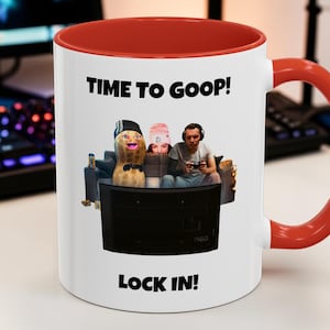 Puede incluir: Taza de cerámica blanca con interior y asa rojos. La taza presenta una imagen de dibujos animados de tres personas viendo la televisión, con el texto "TIME TO GOOP!" arriba y "LOCK IN!" abajo.