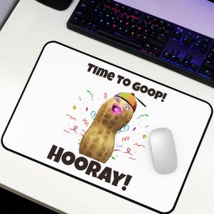 Puede incluir: Alfombrilla de ratón rectangular blanca con borde negro. La alfombrilla presenta un cacahuete de dibujos animados con expresión de sorpresa, con sombrero. El texto en la alfombrilla dice "TIME TO GOOP!" y "HOORAY!" con confeti.