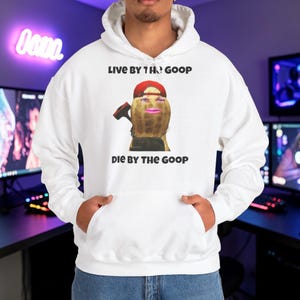 Puede incluir: Sudadera con capucha blanca con un gráfico de un cacahuete con una gorra roja y un martillo. El texto "LIVE BY THE GOOP DIE BY THE GOOP" está impreso encima y debajo del gráfico. La sudadera tiene un bolsillo delantero y una capucha con cordón.