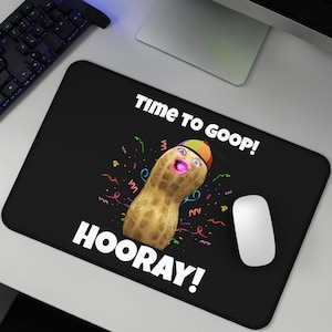 Puede incluir: Alfombrilla de ratón rectangular negra con un personaje de cacahuete de dibujos animados con un gorro de fiesta y confeti. El texto dice "Time to Goop!" y "Hooray!". Un ratón de ordenador blanco está a la derecha.
