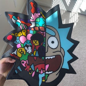 May include: A black, star-shaped decorative piece featuring a split design. One side depicts a colorful, abstract collage, while the other showcases a cartoon character with blue hair and a wide grin. The artwork is vibrant and eye-catching.
