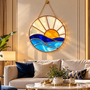 May include: A circular stained glass wall hanging featuring a sunrise over ocean waves. The design includes a bright yellow sun, white sky segments, and layered blue glass waves, all encased in a metallic frame suspended by a gold-toned chain.