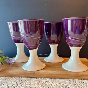 May include: A white ceramic mug with a black handle and the text "But First, Coffee" in a bold, black font. The mug is set against a blurred background, suggesting a cozy setting.