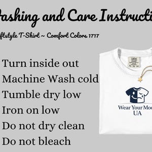 Op de afbeelding: Wit T-shirt met ronde hals, met een afbeelding van een lachend en huilend gezicht. De afbeelding bevat wasvoorschriften en de tekst "Wear Your Mood UA". Het shirt heeft een "Comfort Colors" label. De tekst "Washing and Care Instructions" is ook zichtbaar.