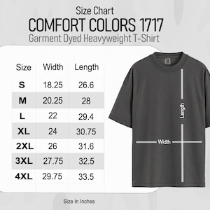 Op de afbeelding: Een donkergrijs Comfort Colors 1717 Garment Dyed Heavyweight T-shirt met een maattabel. De tabel toont maten S tot 4XL, met breedte- en lengtematen in inches. De afmetingen van het shirt worden aangegeven met lijnen.